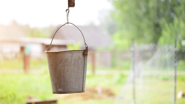 Old metal bucket swinging in the wind around the well in the village yard.
