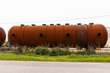 Huge abandoned cistern, worn out by time. Rusty portholes with clearly visible bolts, everything is copper colored with rust, rusty iron. Abandoned portholes, welding industrial constructions.