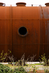 Huge abandoned cistern, worn out by time. Rusty portholes with clearly visible bolts, everything is...