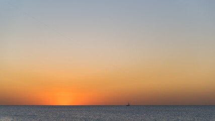 Silhouette of ship on the sea horizon and an airplane flying in the sky above it during beautiful and calm sunset.