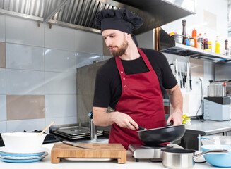 Man is cook. Restaurant chef with frying pan. Culinary guy prepares food. Cafe cook in black chef...