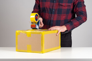 Packaging of goods. Using tape dispenser. Man seals box with tape. Cropped packer from delivery...