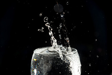 Close-up of a transparent glass cup with water inside and drops making a splash.