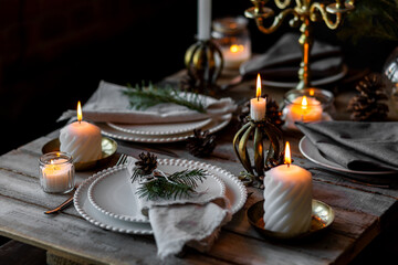 Beautiful table setting for family Christmas dinner at home. Cozy atmosphere, candlelight. Wine glasses, vintage chandelier, elegant interior. Fir tree branches, wooden furniture, dark, bokeh
