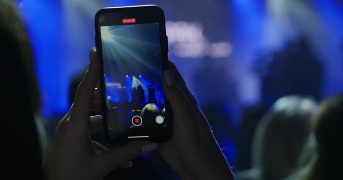 a concert performance by dancers in a dark auditorium, which a person takes a photo or video on his phone. In the frame are the hands of a woman who is filming a performance on her phone. 4k footage