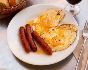 Huevos con chistorra - fried eggs with sausages served with potatoes - obrazy, fototapety, plakaty