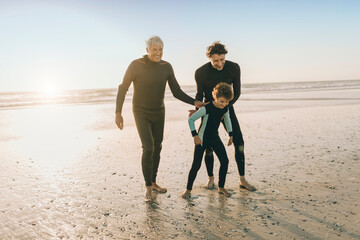 Three generations of men in wetsuits on the beach