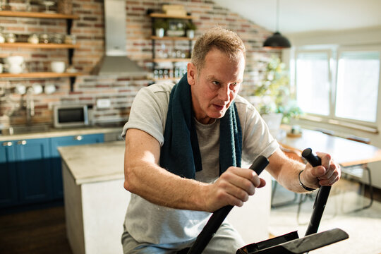 Middle aged man working out on fitness bike at home kitchen