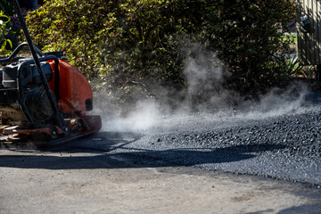 Rammer compacter finishing up the installation of new asphalt in a residential driveway at the...