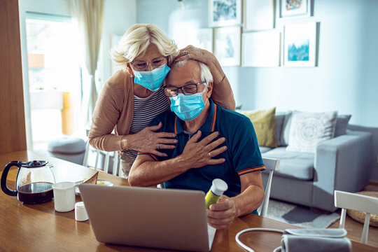 Worried senior couple with masks looking at laptop