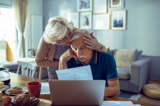 Senior couple reviewing documents and using laptop at home