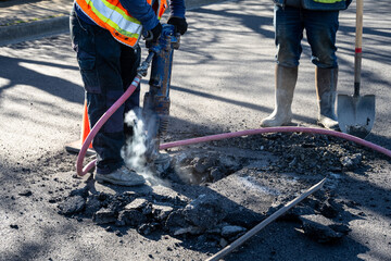 Construction workers using a jackhammer to dig up freshly laid asphalt to find the sewar access...