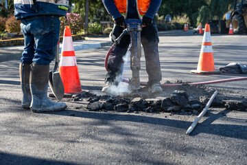 Construction workers using a jackhammer to dig up freshly laid asphalt to find the sewar access...