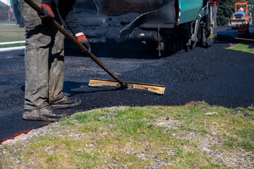 Road crew worker spreading hot asphalt with an asphalt rake at the intersection of a driveway and the street, road construction project
