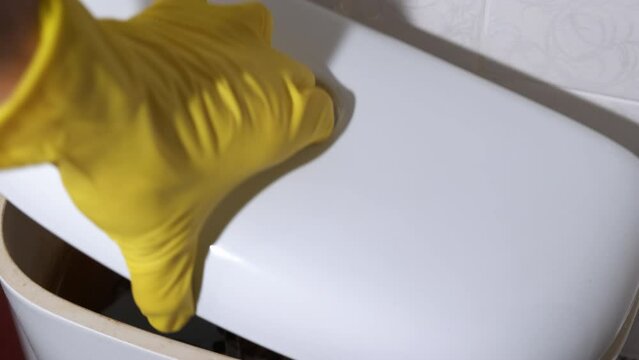Broken toilet barrel. A view of female in protective gloves try to repair the broken toilet cistern indoor.