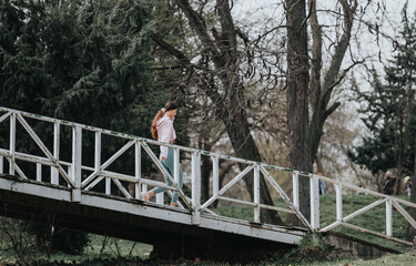 An active woman in sportswear running on an outdoor bridge, surrounded by the tranquility of a leafless park.