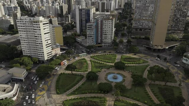 Drone flies slowly to the left from behind red apartment building to reveal Pra&ccedil;a Raul Soares at sunset in Belo Horizonte