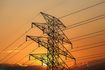 The wires and insulators of a high voltage hydro electricity distribution tower against a sunset sky