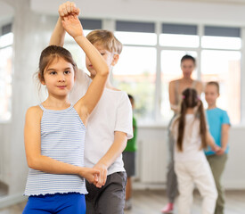Happy preteen children practicing ballroom dances in pairs in training hall during dancing classes