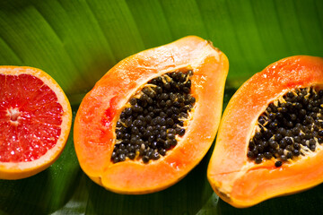 Exotic fruits background. Papaya and orange citrus fresh fruits on tropical leaf green background with shadows of palm tree. Halved fresh organic Papayas and grapefruit exotic fruits close up Top view