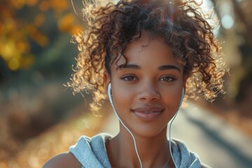 A serene young woman with curly hair enjoys music through earphones on a tranquil autumn day