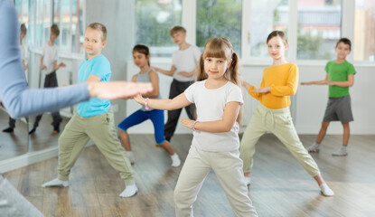 Dynamic little girl training hip hop dance poses with instructor and other attendees of dancing...