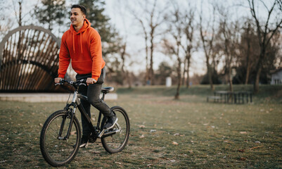 Cheerful young man enjoys a bike ride in a serene park setting as the evening light softens.