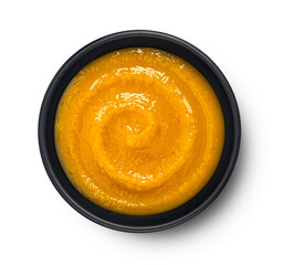 Pumpkin cream soup in black bowl isolated on white background, top view