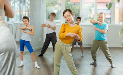 Positive juvenile girl engaged in breakdancing together with children's group in training room during workout session