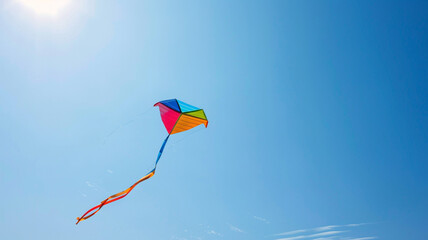 A colorful kite flying high in a clear blue sky on a sunny day.
