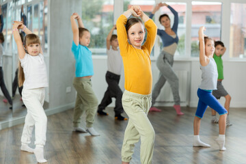 During dance workshop, girl with team of young like-minded children learn to dance modern dances, doing movement with unrecognizable teacher. Studio school for amateur and professional dancers