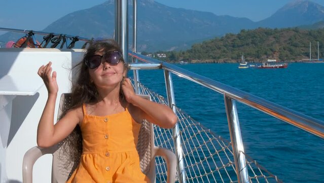 Cute child on a motor boat. Charming little girl is relaxing in sunglasses on the sea deck.