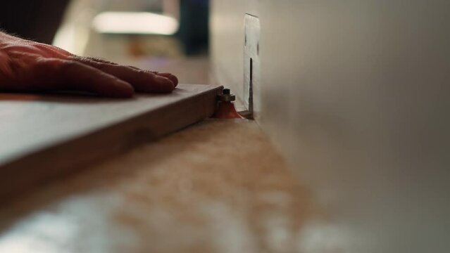 Carpenter in studio puts wood block through spindle moulder, creating smooth edges on wooden pieces. Cabinetmaker in joinery using heavy machinery to craft joints for furniture, camera A close up