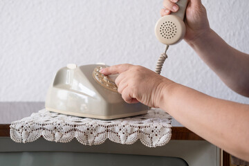 mature female hand removing Handset, rotating Dialer on Old white Rotary Telephone with Disc Dial with finger, putting retro phone reciver down, hanging up, calls helpline, psychological support - obrazy, fototapety, plakaty