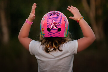 Back view of young girl in sparkly pink bike helmet, arms up in excitement - Powered by Adobe