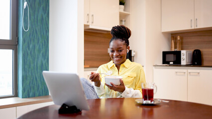 Happy woman having a breakfast and watching something online