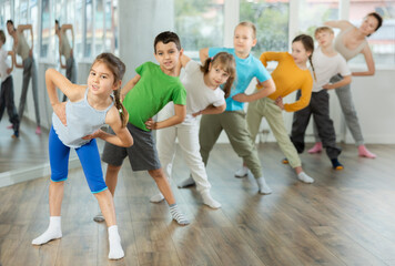 Fototapeta na wymiar Children do warm-up exercises in studio, prepare for pair dance class with teacher. Active lifestyle, extracurricular activities.