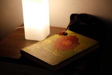 The Quran is on the table near the bedroom lamp
