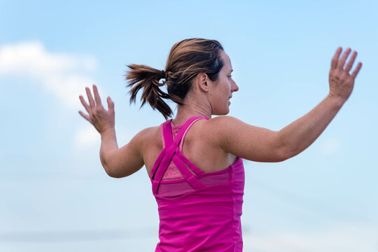 Athletic woman jumping during exercise class outdoors, back view