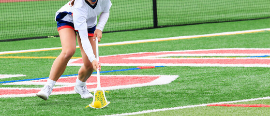 Girls lacrosse player scooping up the ball during a game