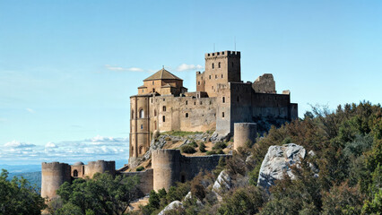 Fototapeta premium loarre castle, an ancient castle located on top of a hill, surrounded by greenery and with a partly cloudy blue sky as a background