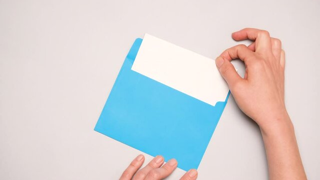 A hand pulls out a white card from a bright blue envelope. Top view of a blue envelope on gray background. Banner for social media ad with copy space.
