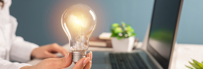 A woman in the office is holding a lit bulb, a symbol of a new idea