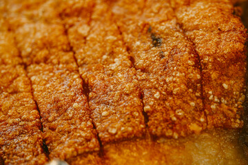 A piece of meat that has been cooked to a crispy, golden brown. The texture of the meat is rough and uneven, with small pieces of fat visible throughout. Scene is one of indulgence and satisfaction