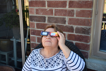 Senior woman watching solar eclipse using special eye glasses - obrazy, fototapety, plakaty