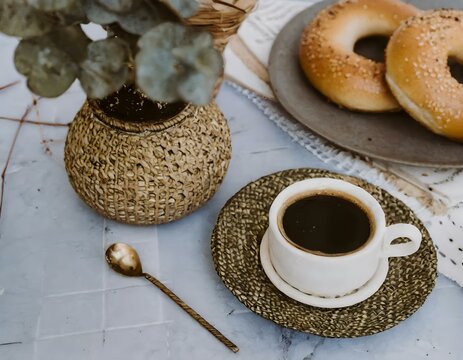 close-up vintage-inspired photo of a cup of coffee, a plate of bagels, and a potted plant with woven accents