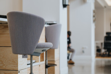 Focused view on a gray office chair in a modern workspace with a blurred background of a person working at their desk.