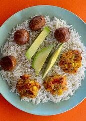 Spicy meatballs with corn fritters and sliced avocado on a bed of basmati rice.