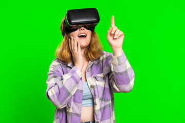 Excited happy adult woman using headset helmet app to play simulation game. Watching virtual reality 3D 360 video. Redhead girl in VR goggles isolated on green chroma key background. Future technology