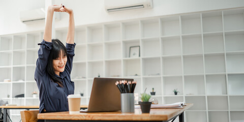 Young businesswoman enjoying a stretching break at her desk to rejuvenate during a busy workday at the office.